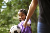 Усміхнена дівчина з футбольним м'ячем тримає руки з матір'ю — стокове фото