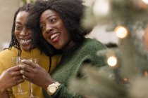 Fröhliche, liebevolle Schwestern, die Wein neben dem Weihnachtsbaum trinken — Stockfoto