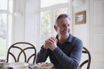 Улыбающийся взрослый мужчина завтракает в современном доме — стоковое фото