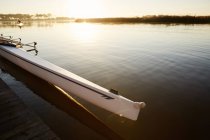 Scull at dock on tranquil sunrise lake — Stock Photo