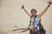 Retrato confiante, despreocupado parapente masculino amarrado com equipamento na praia — Fotografia de Stock