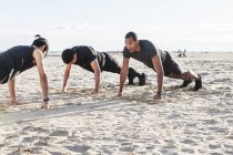 Homens fazendo flexões na praia ensolarada — Fotografia de Stock