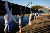 Female rowers lifting scull on sunny lakeside dock — Stock Photo