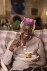 Smiling senior man in Christmas paper crown eating dessert — Stock Photo