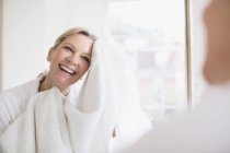 Sorridente donna matura asciugatura viso con asciugamano a specchio bagno — Foto stock