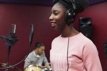 Smiling teenage girl musician recording music, singing in sound booth — Stock Photo