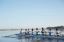 Female rowers rowing scull on sunny lake under blue sky — Stock Photo