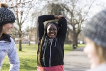 Усміхнена жінка бігунка розтягується в сонячному парку — стокове фото