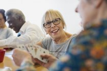 Sorrindo idosa jogando cartas com amigo no centro da comunidade — Fotografia de Stock