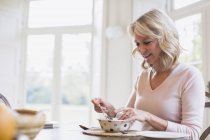 Lächelnde reife Frau frühstückt zu Hause — Stockfoto