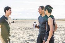 Чоловіки бігуни друзі відпочивають, розмовляють на сонячному пляжі — стокове фото