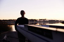 Silhouette of female rower lifting scull on sunrise lakeside dock — Stock Photo