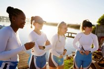 Equipe de remo feminino em pé ao lado do lago ensolarado — Fotografia de Stock