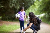 Madre atando cordones de zapatos de hija sosteniendo pelota de fútbol - foto de stock