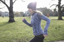 Sorrindo feminino corredor correndo no parque ensolarado — Fotografia de Stock