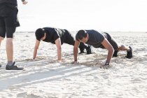 Homens fazendo flexões na praia ensolarada — Fotografia de Stock