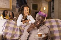 Внучка смотрит, как дедушка в короне ест десерт — стоковое фото
