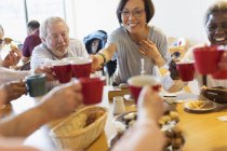 Felices amigos mayores disfrutando del té de la tarde, tazas de tostadas en el centro comunitario - foto de stock