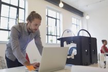 Designer masculino trabalhando no laptop ao lado da impressora 3D no escritório — Fotografia de Stock