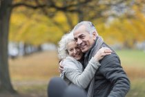 Счастливая старшая пара обнимается в осеннем парке — стоковое фото