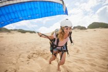 Lächelnde Gleitschirmfliegerin läuft mit Fallschirm am Strand — Stockfoto