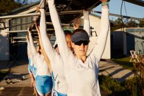 Confident, determined female rowing team lifting scull overhead on sunny dock — Stock Photo
