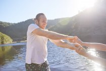 Грайлива пара тримає руки на сонячному літньому озері — стокове фото