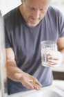 Mature man taking vitamins with glass of water — Stock Photo