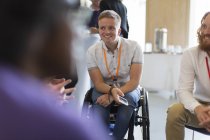 Улыбающаяся женщина в инвалидной коляске разговаривает с коллегами на конференции — стоковое фото