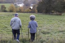 Active senior couple hiking with poles in rural field — Stock Photo