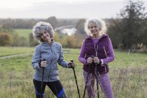 Portrait confident active senior women hikers with poles in rural field — Stock Photo
