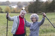 Portrait enthusiastic, confident active senior couple hiking with poles in rural field — Stock Photo