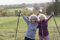 Retrato seguro, entusiasta activo mujeres mayores amigos senderismo con postes en el campo rural - foto de stock