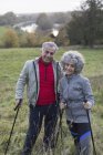 Portrait confident active senior couple hiking with poles in rural field — Stock Photo