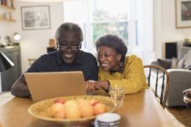 Senior couple using laptop at dining table — Stock Photo