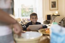 Портрет усміхненого хлопчика, який використовує цифровий планшет на кухні — стокове фото
