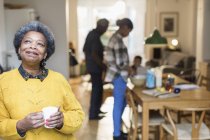 Femme âgée souriante et satisfaite de boire du café en famille en arrière-plan — Photo de stock