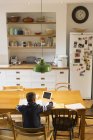 Вид сзади мальчик делает домашнее задание за обеденным столом — стоковое фото
