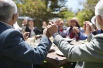 Amis aînés actifs se tenant la main, priant à la table ensoleillée de fête de jardin — Photo de stock