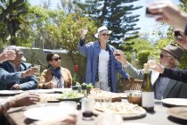 Glückliche Seniorin stößt bei sonnigem Gartenfest mit Freunden auf Wein an — Stockfoto