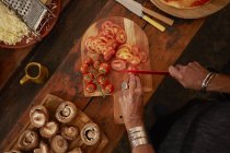Overhead view woman slicing fresh tomatoes for pizza — Stock Photo