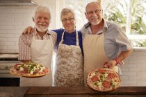 Улыбающиеся портреты, уверенные старшие друзья, готовящие пиццу на уроке кулинарии — стоковое фото