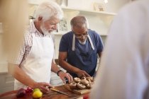 Gli amici anziani tagliano funghi in classe di cucina — Foto stock