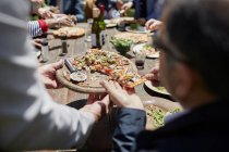Amici che condividono pizza fatta in casa al tavolo soleggiato patio — Foto stock
