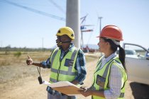 Engineers with blueprints talking at sunny power plant — Stock Photo