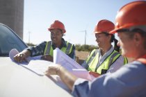 Engineers reviewing blueprints on truck at sunny wind turbine power plant — Stock Photo