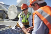 Ingenieros con portapapeles examinan panel solar en planta de energía soleada - foto de stock