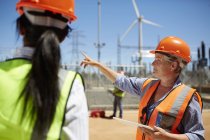 Жінка-інженер з цифровим планшетом розмовляє з колегою на вітроелектростанції — стокове фото