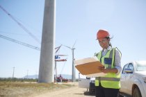 Ingegnere donna sorridente con progetto alla centrale eolica soleggiata — Foto stock