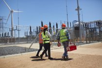 Engenheiros com caixa de ferramentas andando na usina de turbina eólica ensolarada — Fotografia de Stock